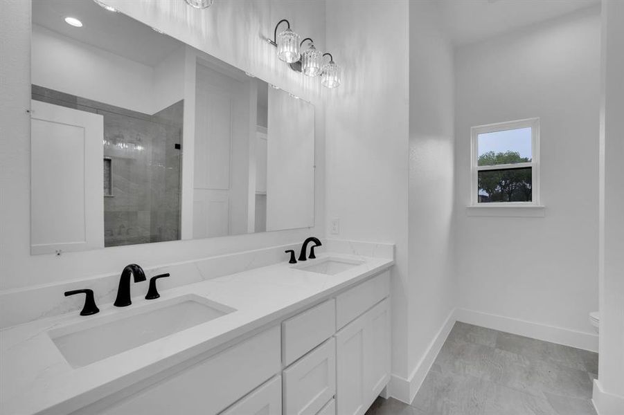 Bathroom featuring tiled shower, dual vanity, tile patterned flooring, and toilet