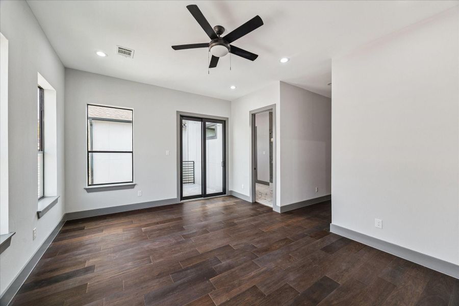 In the primary suite, elegant wood floors, recessed lighting, and a ceiling fan create comfort, while a sliding glass door opens to a private balcony and provides seamless entry to the en suite bathroom. In the primary suite, elegant wood floors, recessed lighting, and a ceiling fan create comfort, while a sliding glass door opens to a private balcony and provides seamless entry to the en suite bathroom.