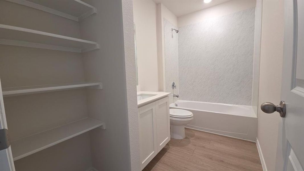 Bathroom featuring a full tub with shower, white vanity with integrated sink, and wood-finish flooring