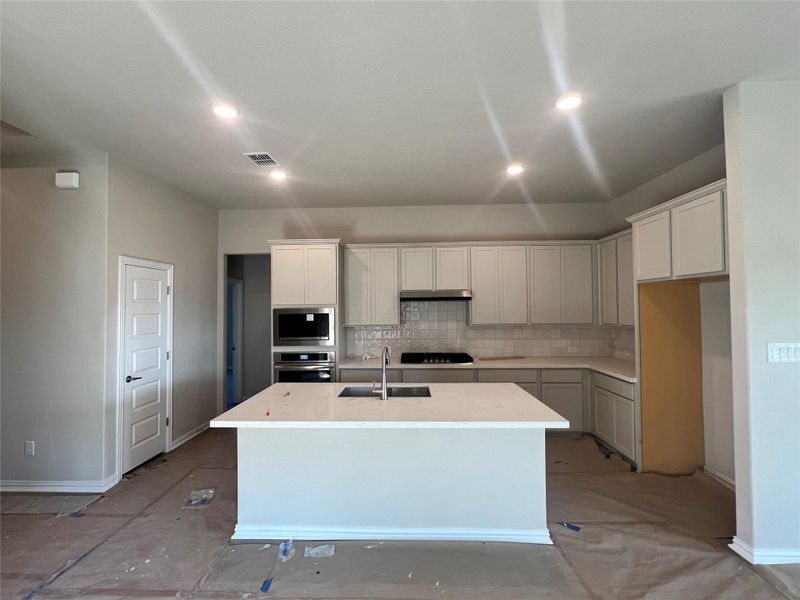 Kitchen featuring decorative backsplash, a center island with sink, appliances with stainless steel finishes, light stone countertops, and recessed lighting