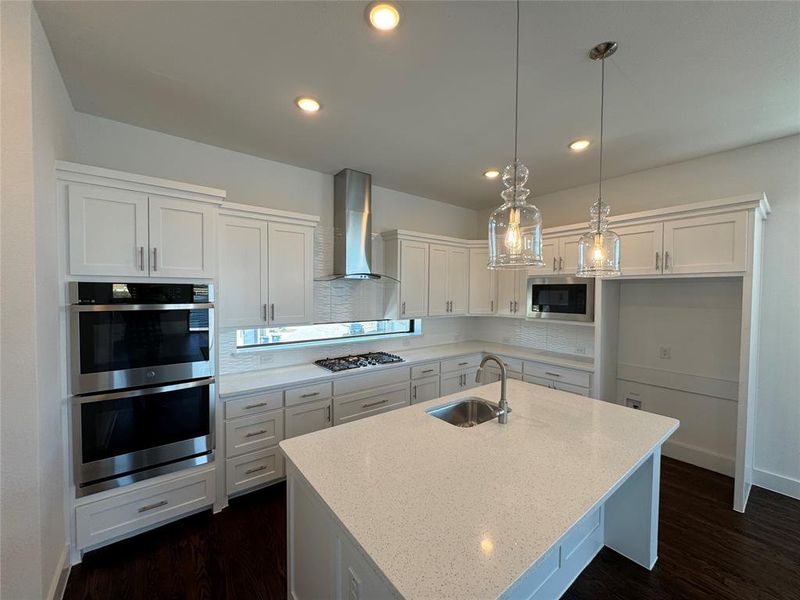 Kitchen featuring white cabinets, wall chimney range hood, sink, and appliances with stainless steel finishes