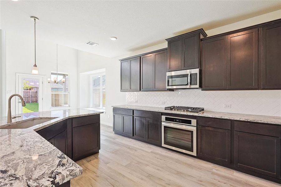 Kitchen with stainless steel appliances, sink, decorative backsplash, light wood-type flooring, and a notable chandelier