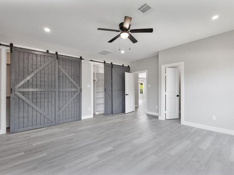 Unfurnished bedroom featuring a barn door, baseboards, light wood-style flooring, recessed lighting, and a spacious closet Unfurnished bedroom featuring a barn door, baseboards, light wood-style flooring, recessed lighting, and a spacious closet