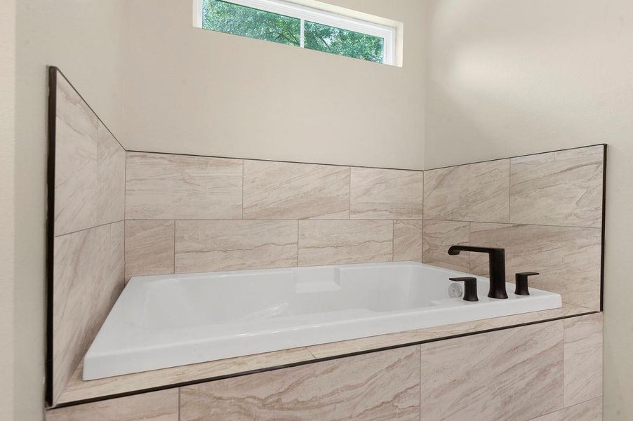 Modern bathroom with a sleek, white tub surrounded by beige marble tiles and featuring stylish black fixtures. A small window above provides natural light. Modern bathroom with a sleek, white tub surrounded by beige marble tiles and featuring stylish black fixtures. A small window above provides natural light.