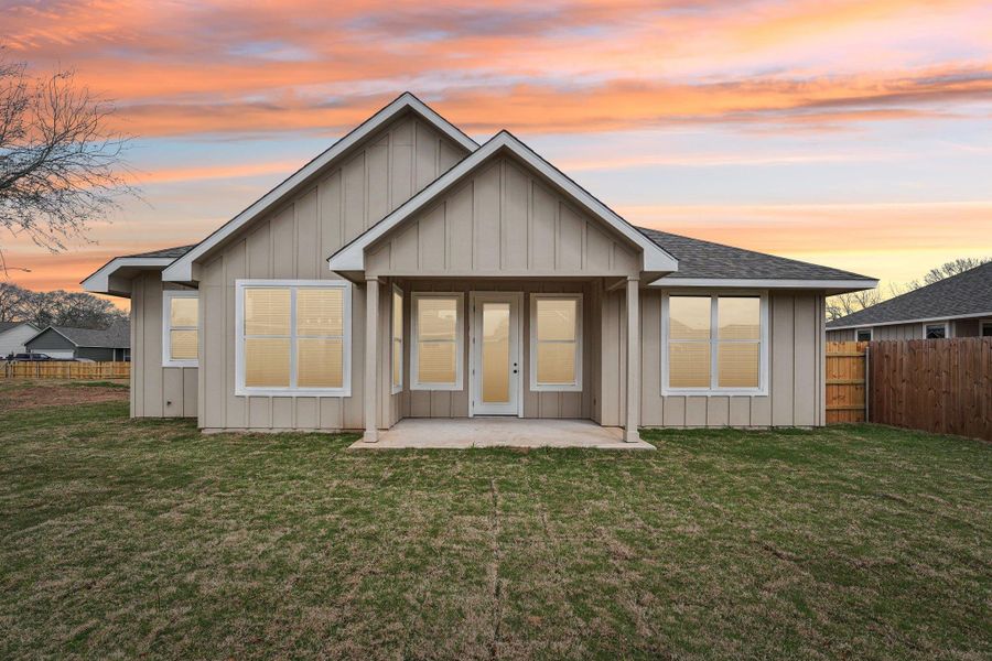 Back of house at dusk featuring a patio area, a yard, fence, and board and batten siding