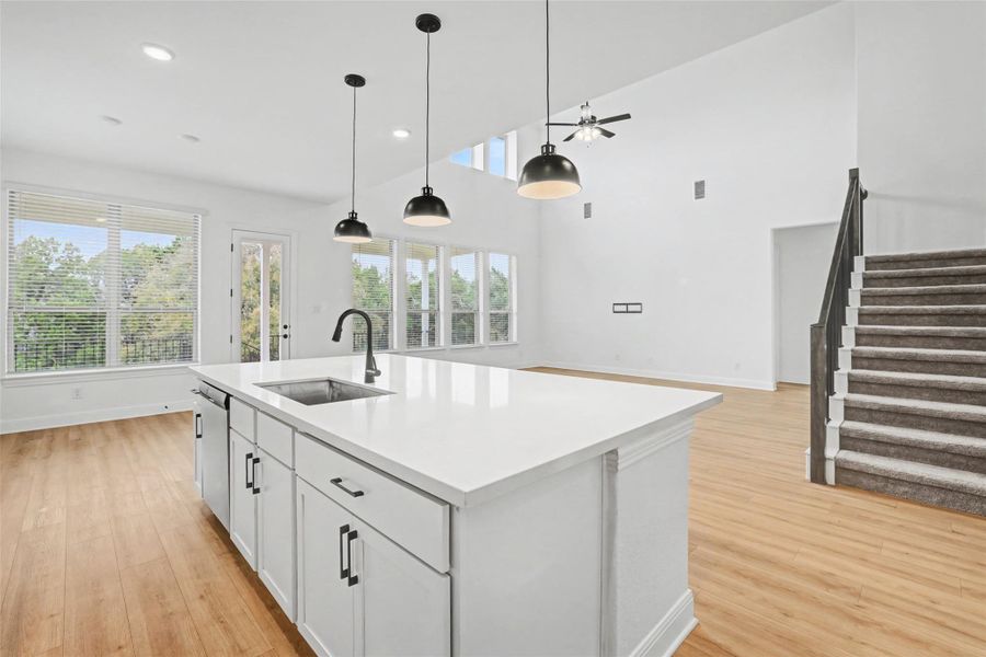 Kitchen featuring decorative light fixtures, white cabinets, light wood-style floors, a kitchen island with sink, and open floor plan