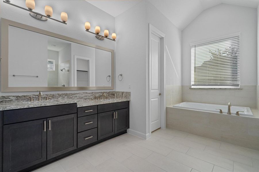 Full bathroom with a bath, double vanity, a shower stall, light tile patterned floors, and vaulted ceiling Full bathroom with a bath, double vanity, a shower stall, light tile patterned floors, and vaulted ceiling