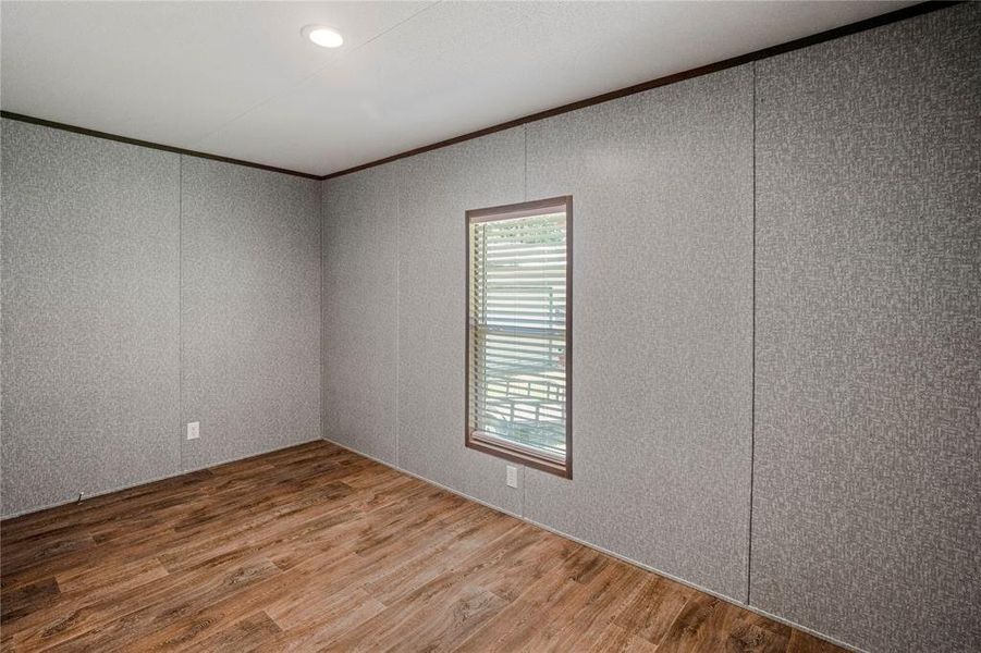 Empty room with crown molding, wood finished floors, and a decorative wall