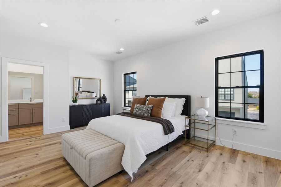 A bright, airy bedroom with modern hardwood floors, a large black-trimmed window.
