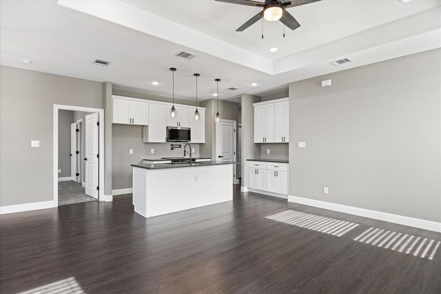 Kitchen with white cabinetry, decorative light fixtures, a kitchen island with sink, and dark wood-type flooring