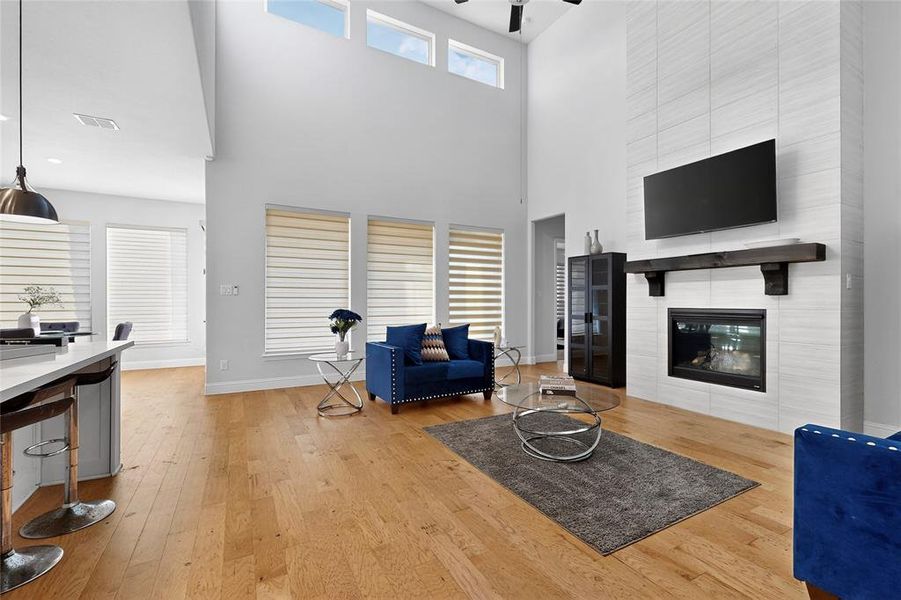 Living area with light wood-type flooring, a fireplace, a high ceiling, and a ceiling fan