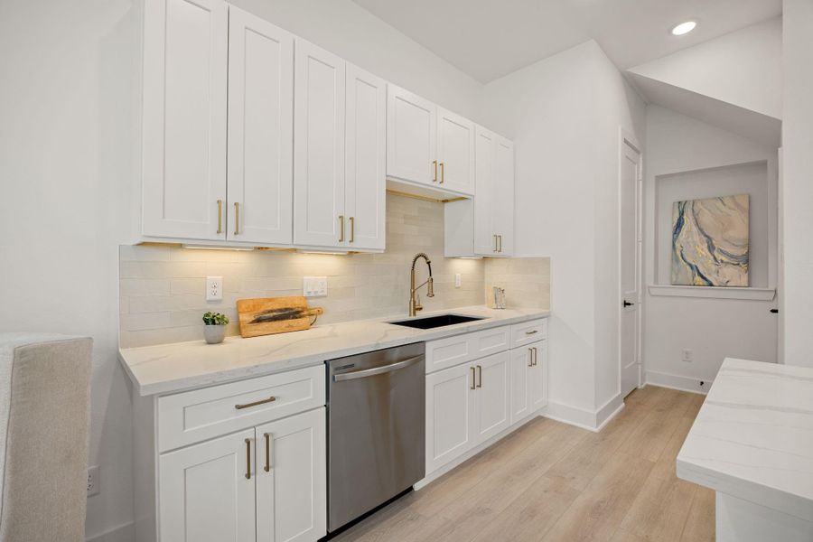 This shot of the kitchen showcases white cabinetry, vinyl wood like flooring, modern tile backsplash, neutral paint and modern finishes. This shot of the kitchen showcases white cabinetry, vinyl wood like flooring, modern tile backsplash, neutral paint and modern finishes.