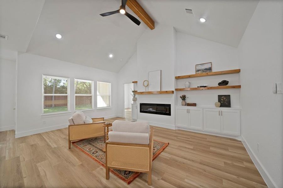 Living area featuring beamed ceiling, high vaulted ceiling, light wood-type flooring, a glass covered fireplace, and recessed lighting