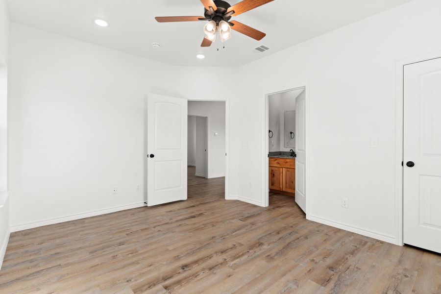 Unfurnished bedroom with visible vents, light wood-style flooring, connected bathroom, and baseboards Unfurnished bedroom with visible vents, light wood-style flooring, connected bathroom, and baseboards