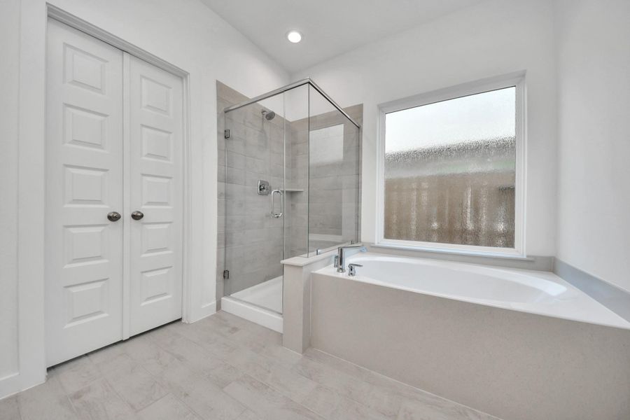 Escape to a spa-like oasis in this primary bathroom. Enjoy a walk-in shower with tile surround, a separate garden tub with custom detailing, and an elegant vanity featuring light countertops, modern hardware, and beautiful recessed lights. Experience luxury and relaxation in every detail. Sample photo of completed home with similar floor plan. Actual colors and selections may vary.