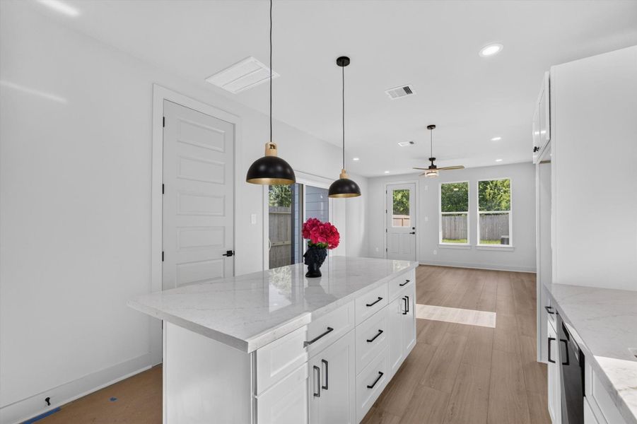 This photo showcases a modern kitchen with clean white cabinetry, a large island with seating, and sleek black pendant lighting. The open layout flows into a bright living area with large windows, hardwood floors, and contemporary furnishings, creating a spacious and inviting atmosphere. This photo showcases a modern kitchen with clean white cabinetry, a large island with seating, and sleek black pendant lighting. The open layout flows into a bright living area with large windows, hardwood floors, and contemporary furnishings, creating a spacious and inviting atmosphere.