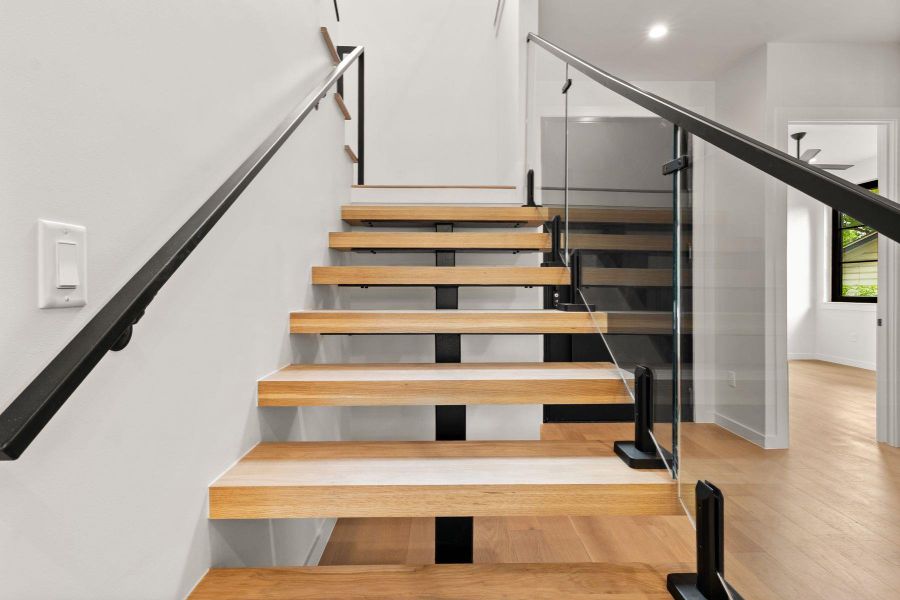 Floating wood stairs with modern glass railings lead upward from the light-filled entryway.