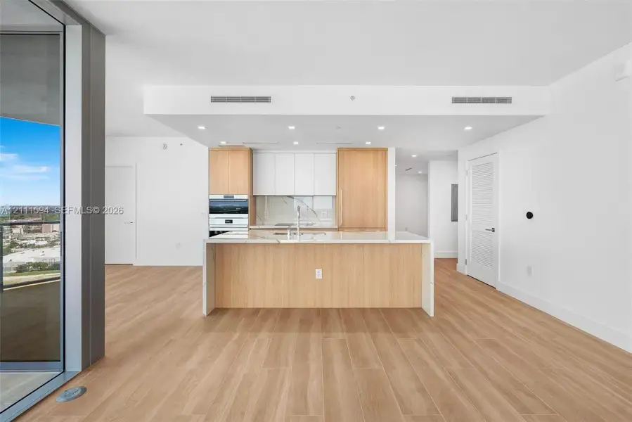 Kitchen featuring wood-finish cabinetry, white slab countertops, a central island, recessed lighting, and integrated wall oven Kitchen featuring wood-finish cabinetry, white slab countertops, a central island, recessed lighting, and integrated wall oven