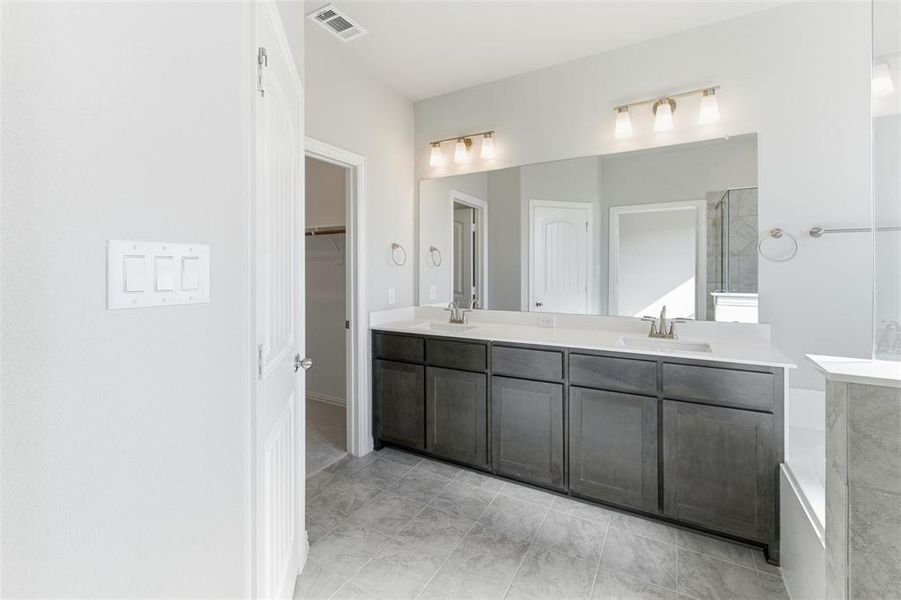 Bathroom with double vanity, a shower stall, a spacious closet, and light tile patterned floors