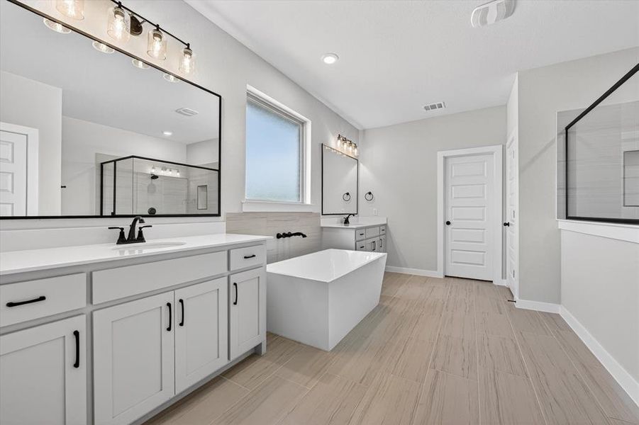 Bathroom featuring dual vanities, a freestanding soaking tub, a separate glass-enclosed shower, wood-finish flooring, and a frosted window
