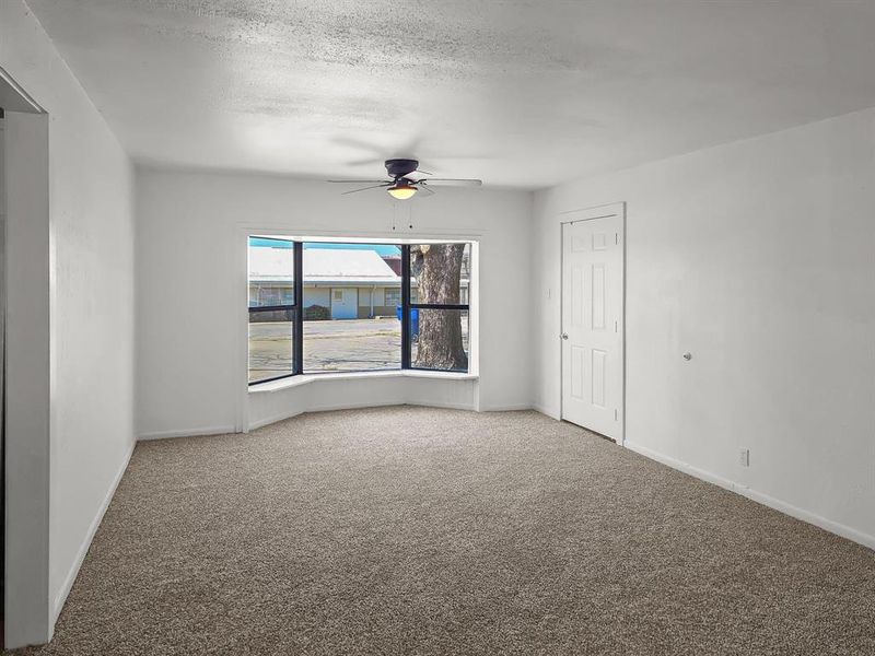 Carpeted livingroom featuring ceiling fan, and Bay Window with side door to covered parking Carpeted livingroom featuring ceiling fan, and Bay Window with side door to covered parking