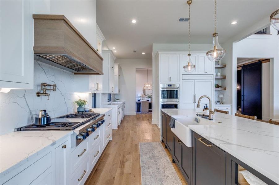 Kitchen featuring white cabinetry, light wood-style flooring, appliances with stainless steel finishes, decorative light fixtures, and light stone countertops Kitchen featuring white cabinetry, light wood-style flooring, appliances with stainless steel finishes, decorative light fixtures, and light stone countertops