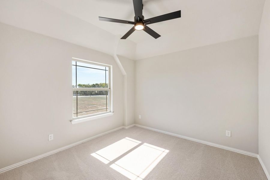 Empty bedroom with vaulted ceiling, black ceiling fan, carpet flooring, and a single window with natural light Empty bedroom with vaulted ceiling, black ceiling fan, carpet flooring, and a single window with natural light