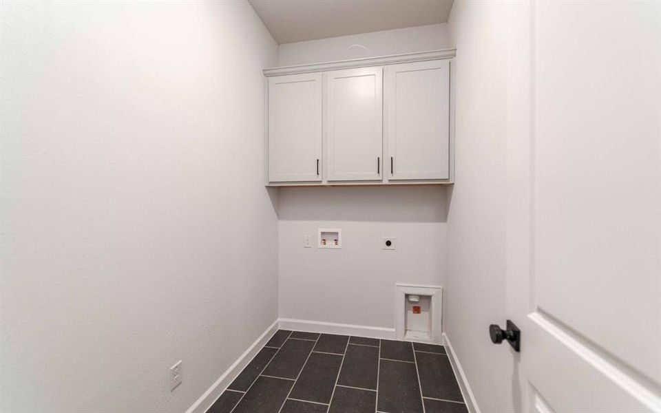 Laundry area featuring dark rectangular floor tiles and light cabinetry Laundry area featuring dark rectangular floor tiles and light cabinetry