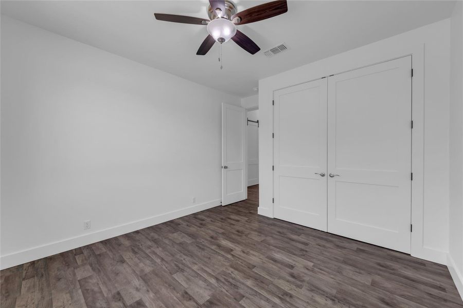 Guest Bedroom 2; Rich wood floors contrast elegantly with crisp white walls and dual-paneled closet doors.