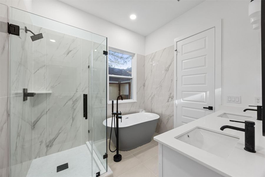 The primary bathroom features a modern design with a glass-enclosed shower, a freestanding tub, and dual sinks. It has elegant marble tile accents, sleek black fixtures, and a bright, airy feel.