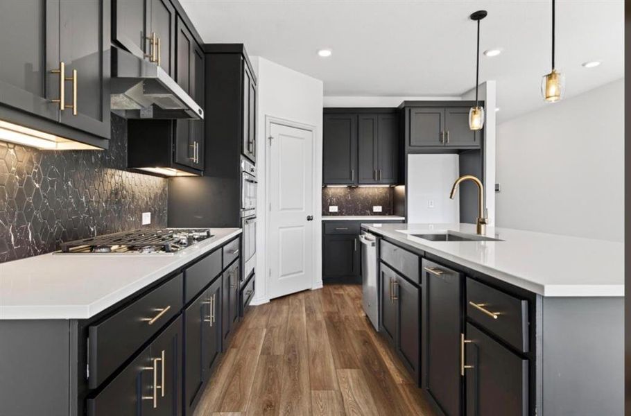 Kitchen with dark wood-style floors, a center island with sink, pendant lighting, decorative backsplash, and under cabinet range hood