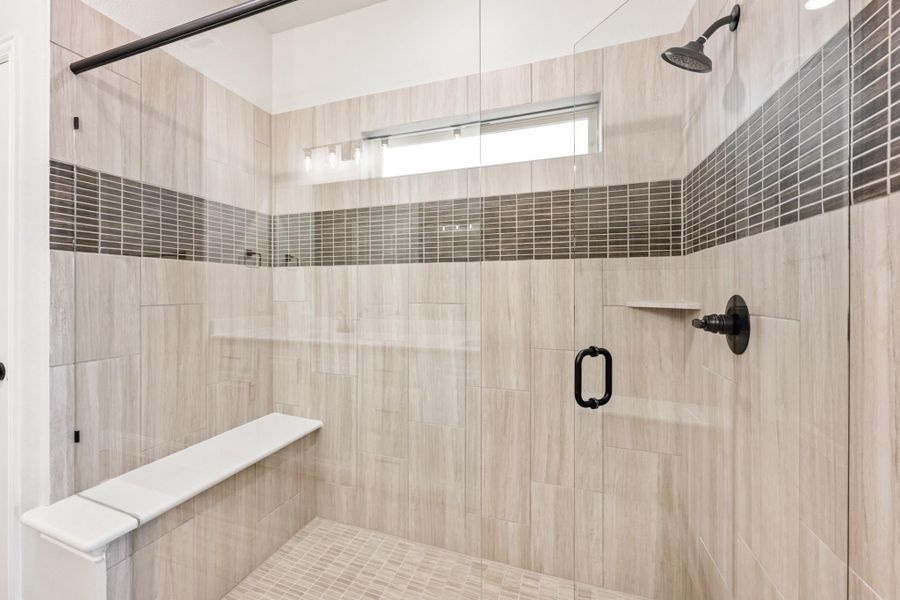 Walk-in shower with glass door, large tile walls, mosaic accent strip, built-in bench, and black fixtures