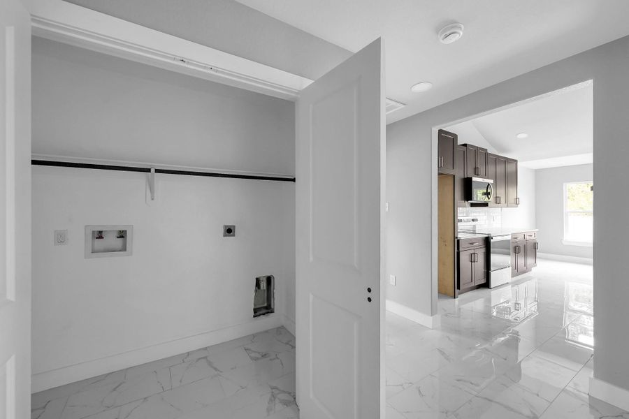 This photo shows a bright, modern laundry area connected to a sleek kitchen with dark cabinetry, stainless steel appliances, and glossy tile flooring.
