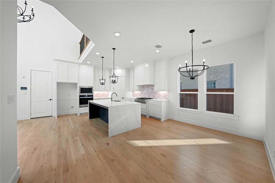 Kitchen featuring a chandelier, white cabinetry, an island with sink, light wood-style floors, and decorative backsplash Kitchen featuring a chandelier, white cabinetry, an island with sink, light wood-style floors, and decorative backsplash
