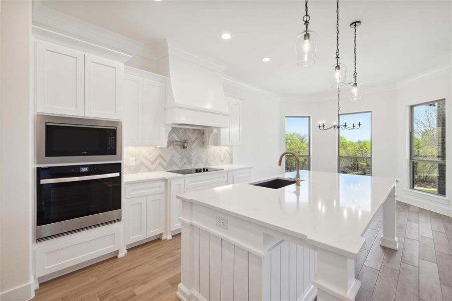 Kitchen featuring custom exhaust hood, built in microwave, oven, sink, and a kitchen island with sink