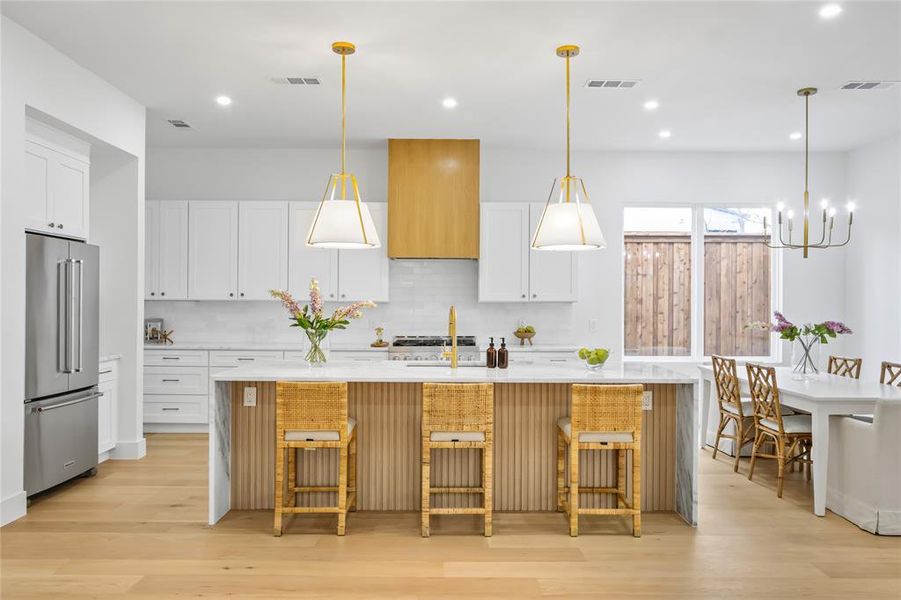 Kitchen with white cabinetry, high end refrigerator, decorative light fixtures, and a kitchen island with sink