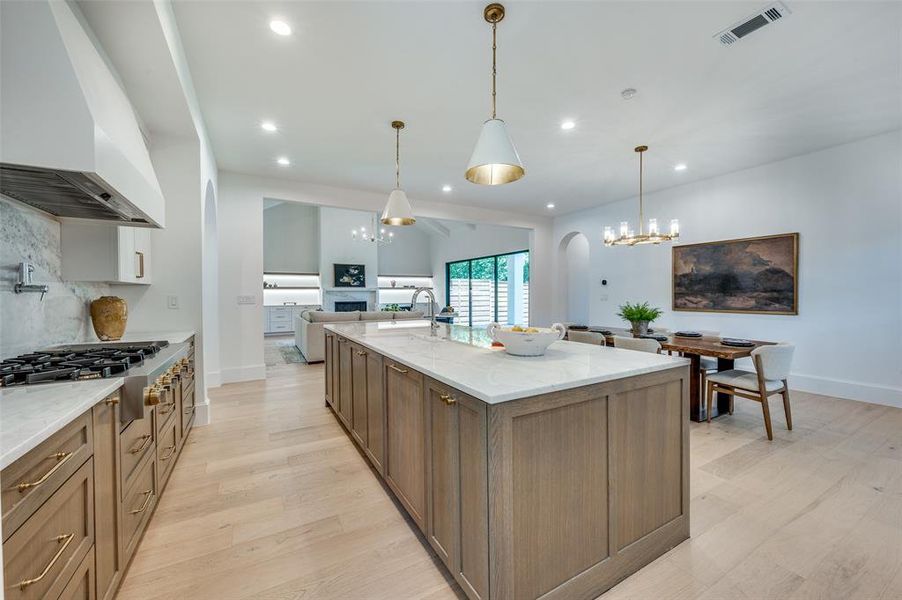 Kitchen featuring custom exhaust hood, stainless steel gas stovetop, recessed lighting, light wood-type flooring, and light stone counters