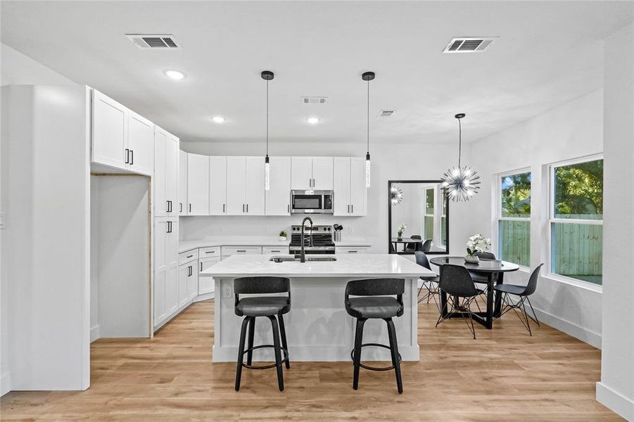 Kitchen with a center island with sink, white cabinets, decorative light fixtures, and light wood-type flooring