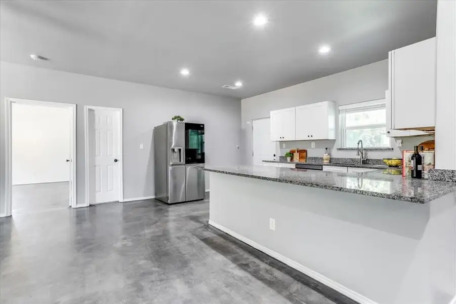 Modern kitchen featuring a granite-topped island with breakfast bar, white cabinetry, a stainless steel refrigerator, and recessed lighting