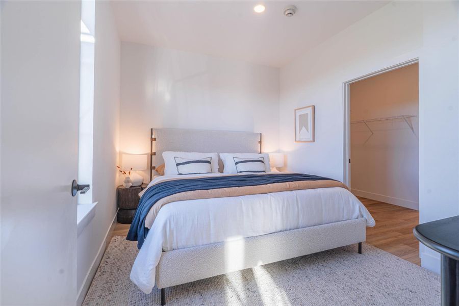 Bedroom with a walk in closet and light wood-style floors.Photos shown are of a model residence and are representative in nature. Actual residence may differ in layout, finishes, and views.