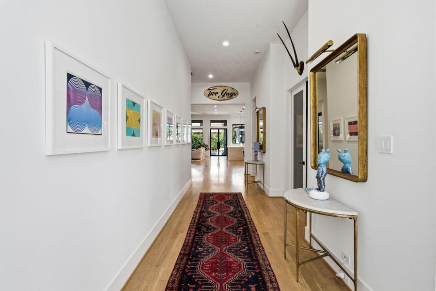 Elegant gallery-style hallway with clean lines, art display walls, and warm wood flooring, leading seamlessly into the main living spaces.