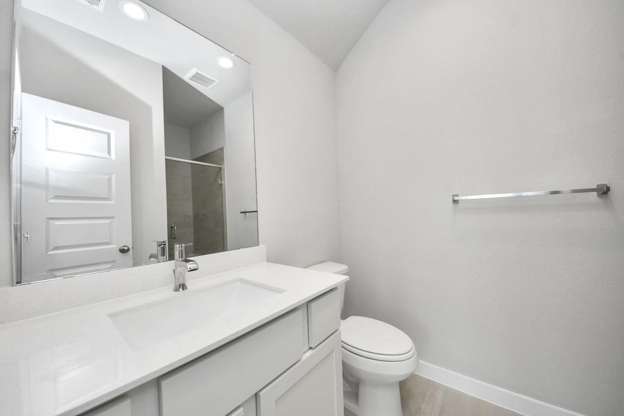 Secondary bath features tile flooring, a walk-in shower with tile surround, light stained wood cabinets, beautiful light countertop. Sample photo of completed home with similar floor plan. Actual colors and selections may vary.