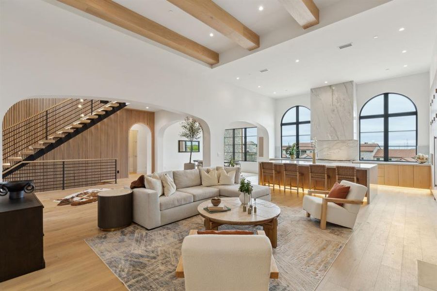 Living room featuring arched walkways, stairway, beamed ceiling, white oak wood flooring, wood accents on wall, Floating staircase, iron hand rail , and a high ceiling Living room featuring arched walkways, stairway, beamed ceiling, white oak wood flooring, wood accents on wall, Floating staircase, iron hand rail , and a high ceiling