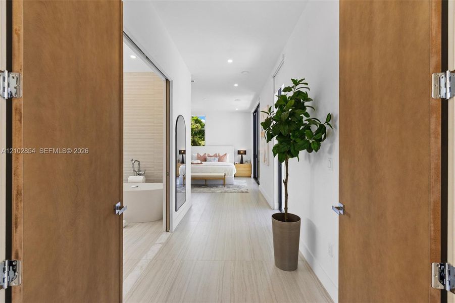 Double wood-finish doors opening to a space with neutral large-format tile flooring, recessed lighting, and a freestanding soaking tub