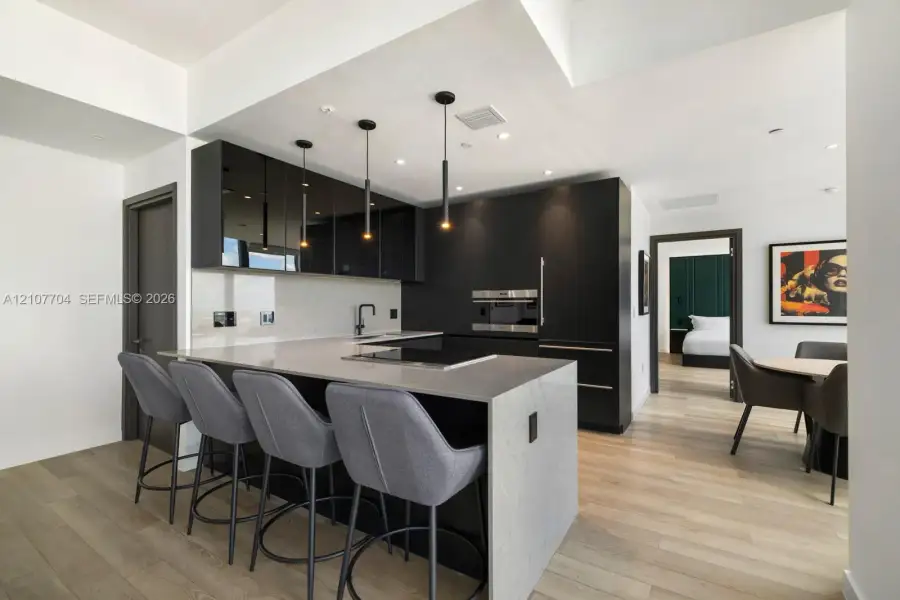 Kitchen featuring high-gloss black cabinetry, light-toned stone countertops, integrated cooktop, built-in wall oven, and pendant lighting