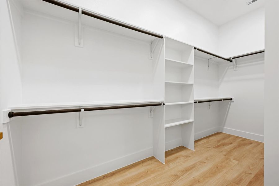 Walk-in closet featuring white walls, multi-level shelving, dark-finish hanging rods, and wood-finish flooring