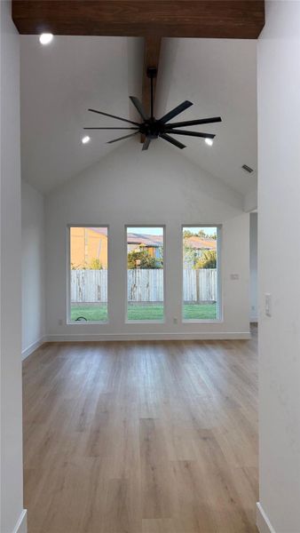 Vaulted living room with wood beams and ceiling fan. Large windows for natural light.