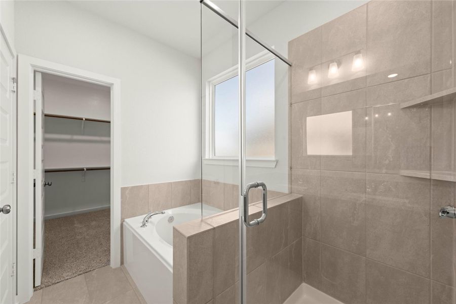 Luxurious bathing retreat boasts a soaking tub, glass-enclosed shower, and convenient walk-in closet access.