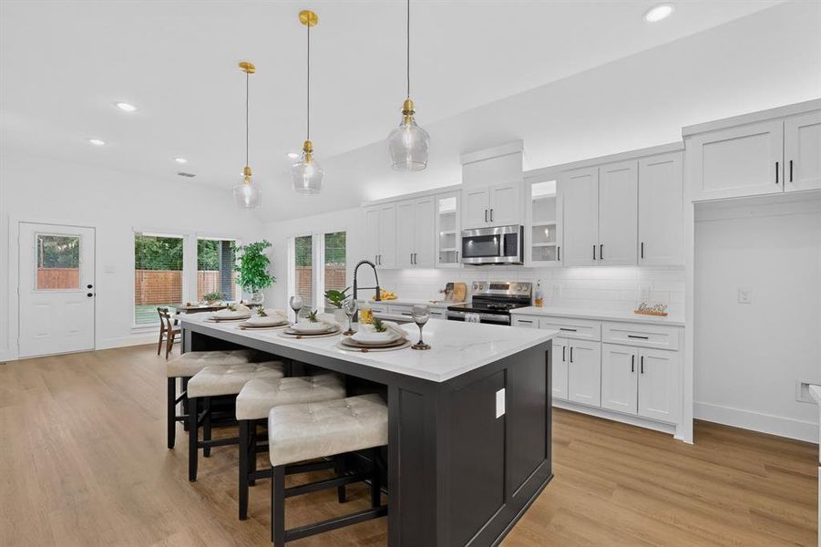 Open-concept kitchen featuring a large island with white stone-finish countertop, white cabinetry with contemporary hardware, stainless steel microwave, and wood-finish flooring