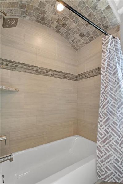 Full bath featuring lofted ceiling, brick ceiling, and shower / bath combo